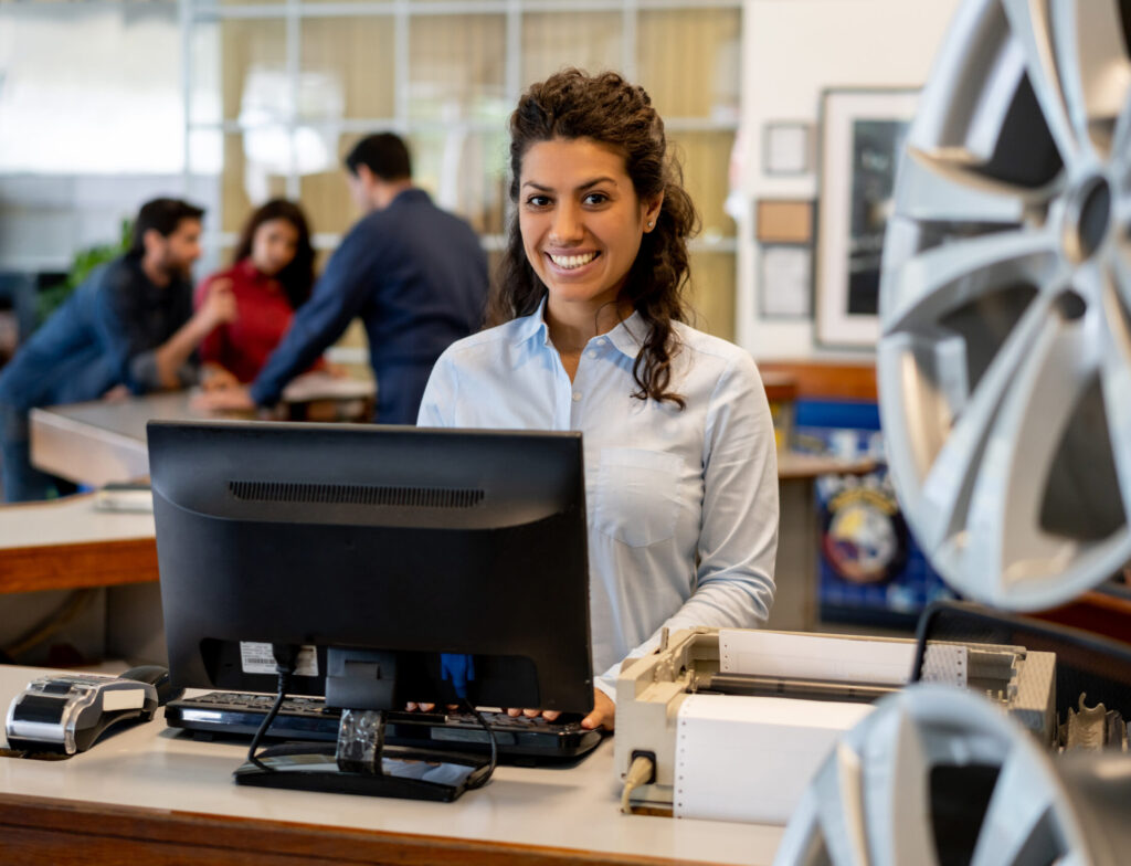 beautiful young female sales clerk at a car workshop smiling at camera standing behind counter